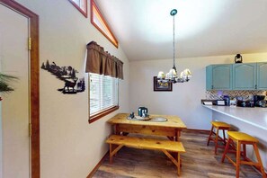 A compact kitchen with a wooden table, bench seating, and a hanging light fixture. - Horseshoe Haven - Mountain-View Home • Deck & Grill (Divide)