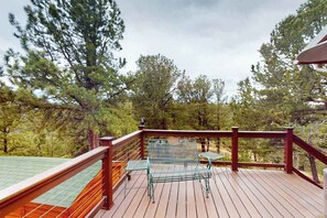 A wooden deck with metal chairs and a table, surrounded by trees. - Horseshoe Haven - Mountain-View Home • Deck & Grill (Divide)