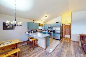 A modern kitchen with a central island, light blue cabinets, stainless steel appliances, and a wooden dining table with stools. - Horseshoe Haven - Mountain-View Home • Deck & Grill (Divide)