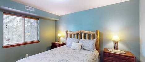 A bedroom with a bed, two bedside tables with lamps, a window with blinds, and a ceiling light.