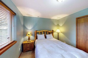 Un dormitorio con cama, mesita de noche, lámpara, ventana con persianas y puerta.