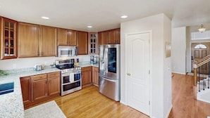 A kitchen with wooden cabinets, stainless steel appliances, and a white door. - Jack’s Ranch House- Family Home • Game Room & Mtn Views (Colorado Springs)