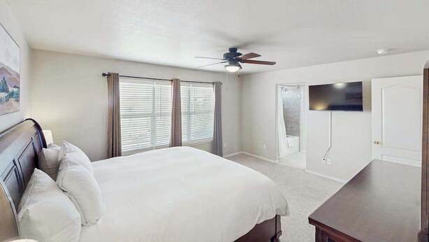 A bedroom with a bed, a ceiling fan, a TV mounted on the wall, and a door. - Jack’s Ranch House- Family Home • Game Room & Mtn Views (Colorado Springs)