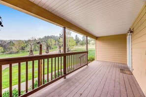 A covered porch with a wooden railing, a view of a green landscape, and a clear sky. - Hot Springs - Spacious 4 Bedroom Home with Patio (Hot Springs)
