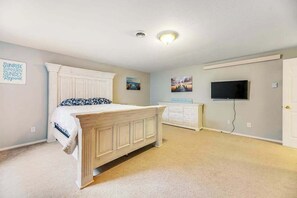 A bedroom with a bed, a dresser, a television, and a wall-mounted shelf.