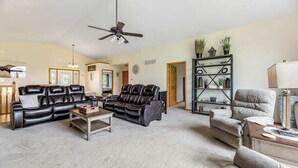 Ein Wohnzimmer mit schwarzem Ledersofa, einem beigen Sessel, einem Couchtisch und einem Bücherregal.