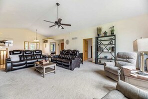 Ein Wohnzimmer mit schwarzem Ledersofa, einem beigen Sessel, einem Couchtisch und einem Bücherregal.