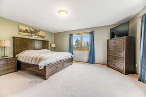 A bedroom with a large bed, a dresser, a television on a stand, and a window with curtains. - Hot Springs - Spacious 4 Bedroom Home with Patio (Hot Springs)