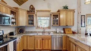 A kitchen with wooden cabinets, a stainless steel dishwasher, and a window with a view of trees. - Legacy Lodge - 4BR Lodge Minutes from Deadwood (Sturgis)