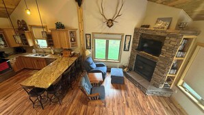 A spacious living area with a stone fireplace, a large wooden ceiling, and a kitchen with a granite countertop. - Legacy Lodge- 4BR Lodge Minutes from Deadwood (Sturgis)