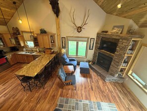 A spacious living area with a stone fireplace, a large wooden ceiling, and a kitchen with a granite countertop. - Legacy Lodge- 4BR Lodge Minutes from Deadwood (Sturgis)