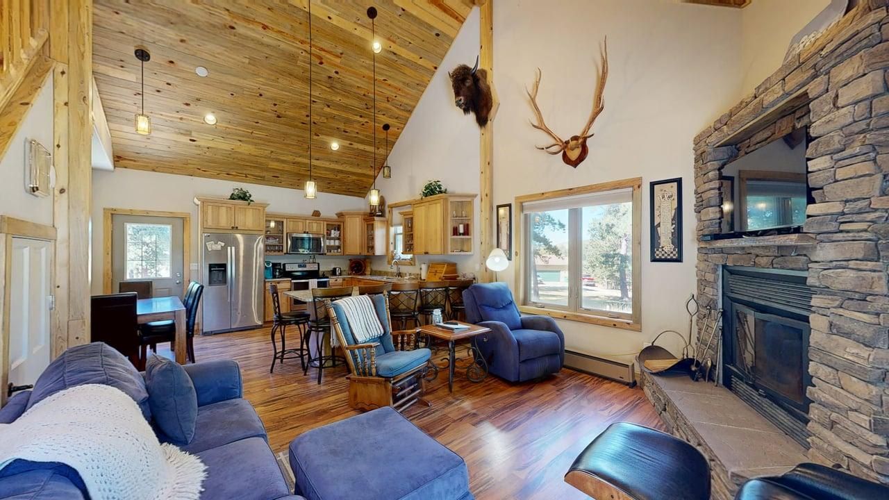 A cozy living room with a fireplace, wooden ceiling, and a dining area with a table and chairs.