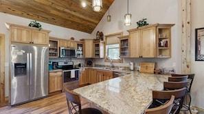 A kitchen with wooden cabinets, stainless steel appliances, granite countertops, and a bar seating area. - Legacy Lodge - 4BR Lodge Minutes from Deadwood (Sturgis)