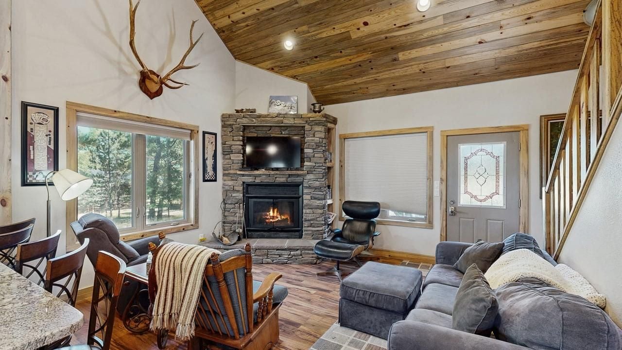 A cozy living room with a stone fireplace, a television, and a large window.