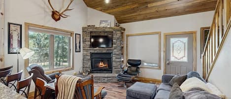 Una sala de estar acogedora con chimenea de piedra, televisor y un ventanal grande.