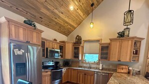 A kitchen with wooden cabinets, a stainless steel refrigerator, a built-in oven, and a dining area with a wooden table and chairs. - Legacy Lodge- 4BR Lodge Minutes from Deadwood (Sturgis)