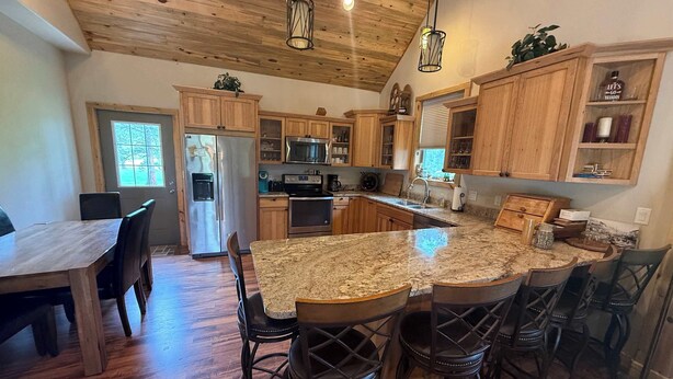 A spacious kitchen with wooden cabinets, a granite countertop, and a dining area with chairs. - Legacy Lodge- 4BR Lodge Minutes from Deadwood (Sturgis)