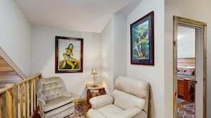 A room with a wooden staircase, two leather armchairs, a small table with a lamp, and two framed pictures on the wall. - Legacy Lodge - 4BR Lodge Minutes from Deadwood (Sturgis)