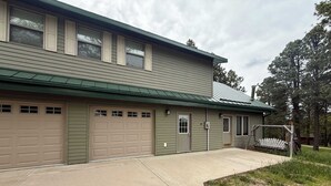 A two-story building with a green exterior, a garage with multiple doors, and a covered porch area. - Legacy Lodge- 4BR Lodge Minutes from Deadwood (Sturgis)