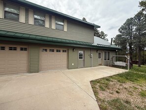 A two-story building with a green exterior, a garage with multiple doors, and a covered porch area. - Legacy Lodge- 4BR Lodge Minutes from Deadwood (Sturgis)