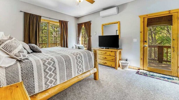 A bedroom with a bed, a TV, a ceiling fan, and a large window. - Lazy Bear Lodge - Rustic Lodge • Hot Tub & Wrap Deck (Sturgis)