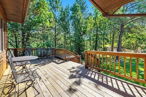 A wooden deck with a table and chairs, surrounded by a forest. - Lazy Bear Lodge - Rustic Lodge • Hot Tub & Wrap Deck (Sturgis)