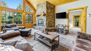 A spacious living area with a stone fireplace, leather sofas, and a television mounted on the wall. - Lazy Bear Lodge - Rustic Lodge • Hot Tub & Wrap Deck (Sturgis)