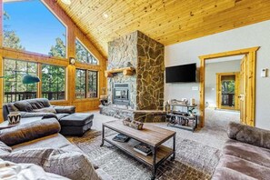 A spacious living area with a stone fireplace, leather sofas, and a television mounted on the wall. - Lazy Bear Lodge - Rustic Lodge • Hot Tub & Wrap Deck (Sturgis)