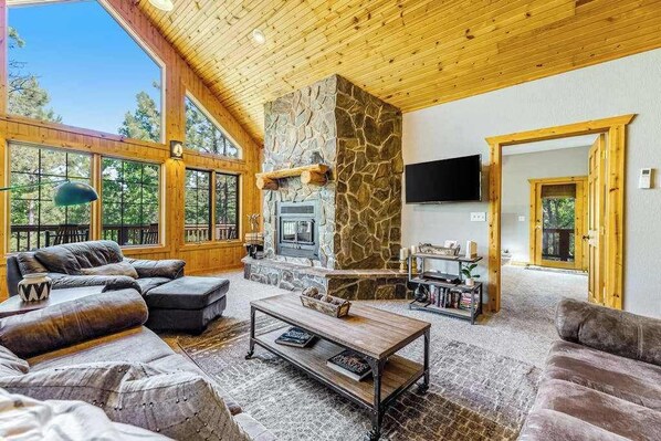 A spacious living area with a stone fireplace, leather sofas, and a television mounted on the wall. - Lazy Bear Lodge - Rustic Lodge • Hot Tub & Wrap Deck (Sturgis)