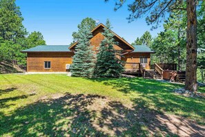 A log cabin with a green roof, surrounded by a grassy yard and trees. - Lazy Bear Lodge - Rustic Lodge • Hot Tub & Wrap Deck (Sturgis)