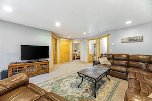 A living room with a television, leather sofas, a coffee table, and a patterned rug. - Lazy Bear Lodge - Rustic Lodge • Hot Tub & Wrap Deck (Sturgis)