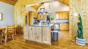 A rustic kitchen with wooden cabinets, a central island, and a hanging light fixture. - Lazy Bear Lodge - Rustic Lodge • Hot Tub & Wrap Deck (Sturgis)