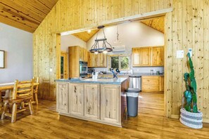 A rustic kitchen with wooden cabinets, a central island, and a hanging light fixture. - Lazy Bear Lodge - Rustic Lodge • Hot Tub & Wrap Deck (Sturgis)