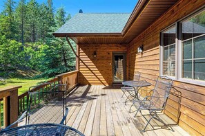 A wooden cabin with a deck, two metal chairs, and a table. - Lazy Bear Lodge - Rustic Lodge • Hot Tub & Wrap Deck (Sturgis)