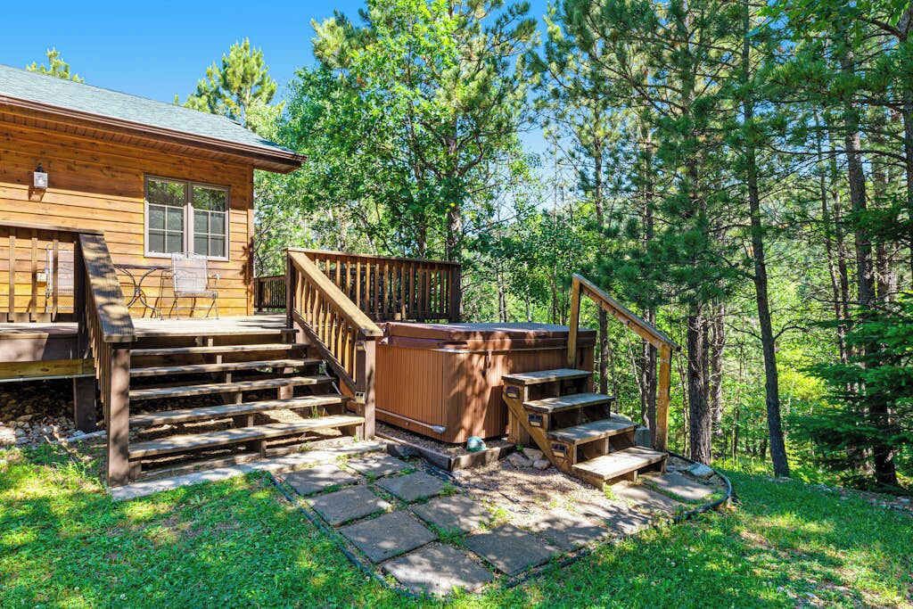 A wooden cabin with a deck, outdoor seating, and a hot tub.