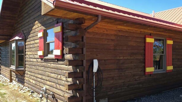 Eine Holzhütte mit geneigtem Dach, einem Fenster mit rotem Rollo und einer Metallantenne.