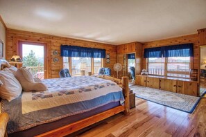Un dormitorio de cabaña de madera con una cama grande, un ventilador y vistas al exterior.