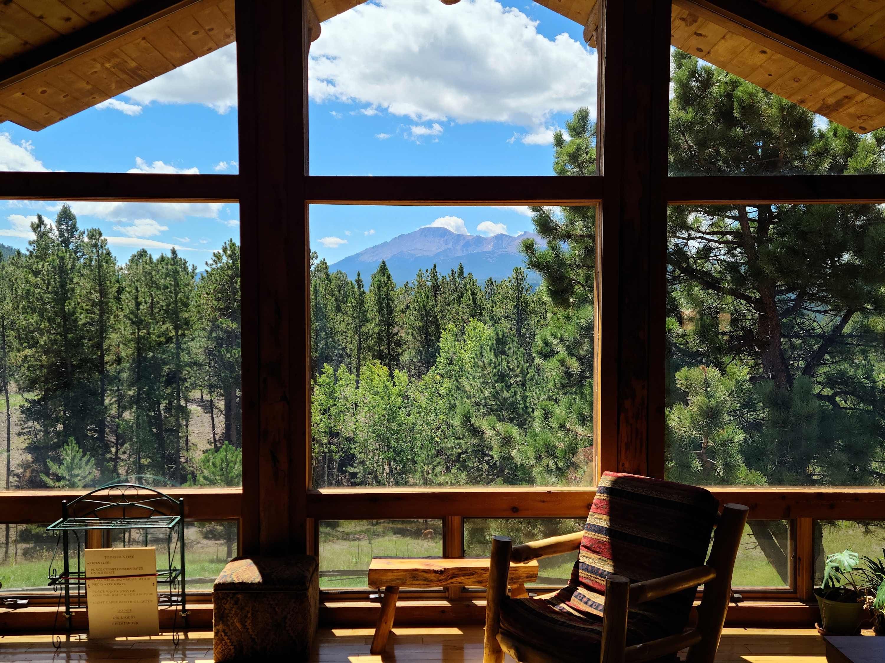 Une cabane en bois dotée de grandes fenêtres qui offrent une vue sur une forêt et une montagne.