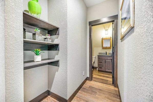 A hallway with a textured wall, wooden flooring, and a kitchen area visible through an open door. - Pillar Peak Perch - Luxury Lodge • Hot Tub & Big Views (Sturgis)