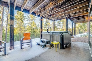 An outdoor covered area with a hot tub, seating, and a view of trees. - Pillar Peak Perch - Luxury Lodge • Hot Tub & Big Views (Sturgis)
