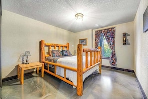 A bedroom with a wooden bed, a bedside table, and a window with patterned curtains. - Pillar Peak Perch - Luxury Lodge • Hot Tub & Big Views (Sturgis)