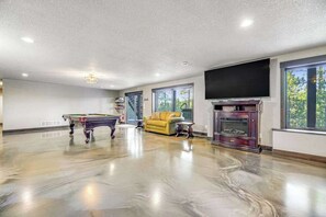 A spacious room with a billiards table, a yellow sofa, and a fireplace. - Pillar Peak Perch - Luxury Lodge • Hot Tub & Big Views (Sturgis)