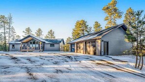 Ein zweistöckiges Gebäude mit Veranda und Garage, umgeben von schneebedecktem Boden und Bäumen.