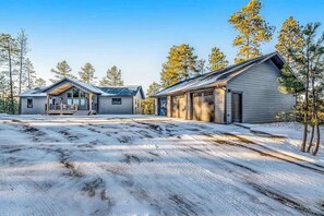 A two-story building with a porch and garage, surrounded by snow-covered ground and trees. - Pillar Peak Perch - Luxury Lodge • Hot Tub & Big Views (Sturgis)