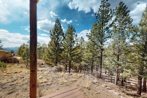 A wooden deck leading into a forested area with tall pine trees and a clear sky. - Peak View Vista - Secluded Home • Mtn Views on 5 Acres (Florissant)