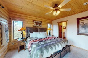 A log cabin bedroom with a bed, two bedside lamps, a ceiling fan, and a bear-themed wall decoration. - Peak View Vista - Secluded Home • Mtn Views on 5 Acres (Florissant)