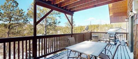 A wooden deck with a table and chairs, overlooking a forested area.