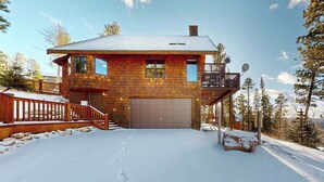 Eine zweistöckige Blockhütte mit Garage, Balkon und einem verschneiten Einfahrt.