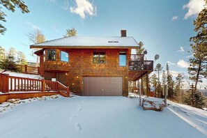 Eine zweistöckige Blockhütte mit Garage, Balkon und einem verschneiten Einfahrt.