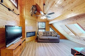 Ein gemütliches Zimmer mit Fernseher, Sofa und Deckenventilator.